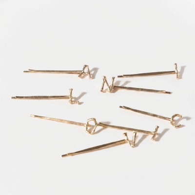 
                    
                      Peignee Paris Alphabet Letter gold-plated steel hair clips, featuring textured letters, scattered flat lay on white.
                    
                  