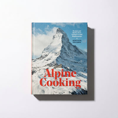 
                    
                      Alpine Cooking cookbook, full cover view of snowy mountain and blue sky, with red title text, slight overhead angle.
                    
                  