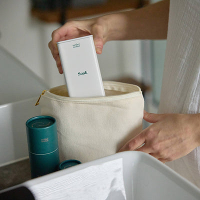 
                    
                      Mother Mother Magnesium Bath Soak, white tin being packed into a natural canvas bag, with teal container.
                    
                  