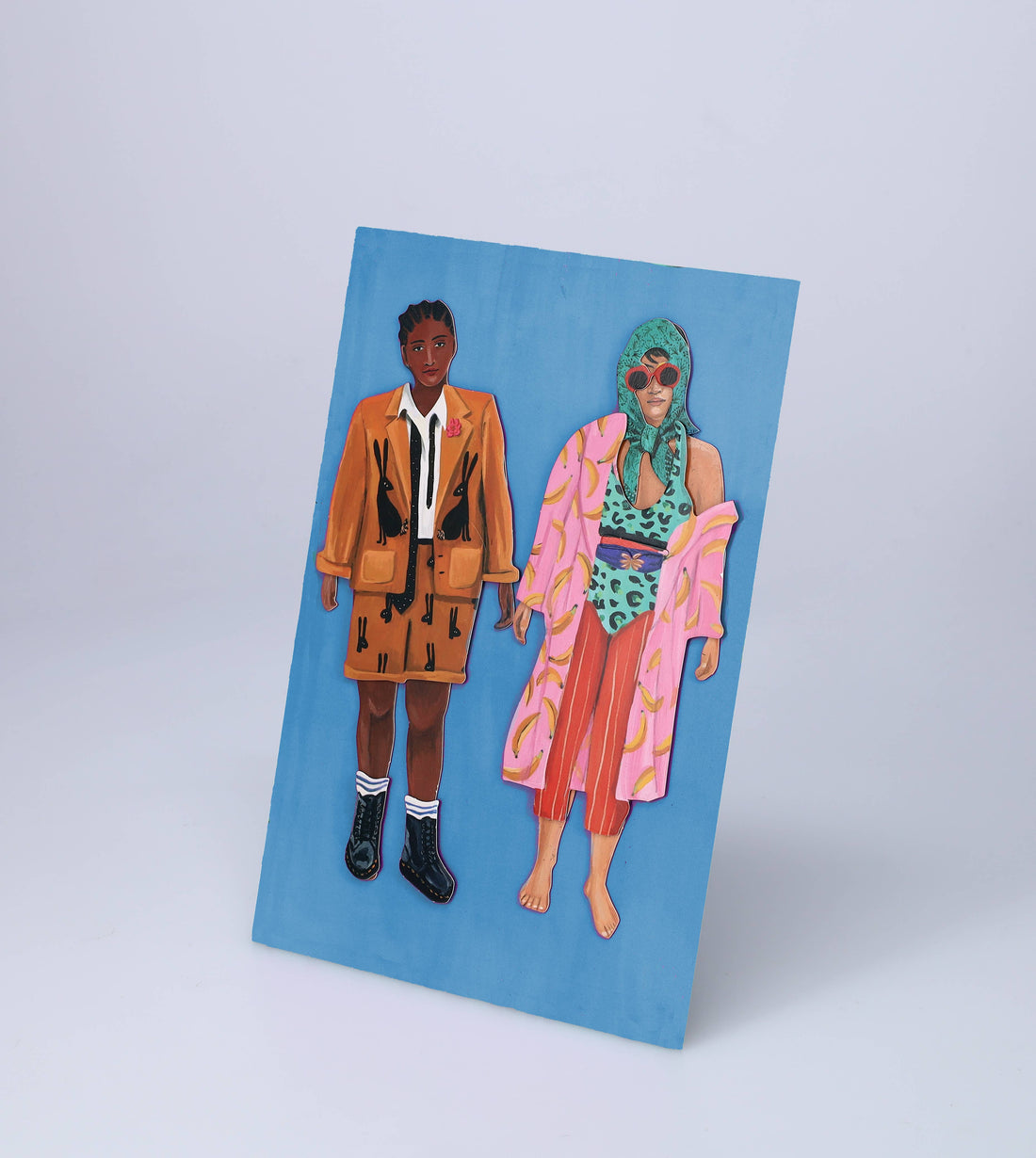 Fearless Fashion magnetic dolls: two paper figures, one in orange rabbit jacket, one in pink banana robe, angled on blue.