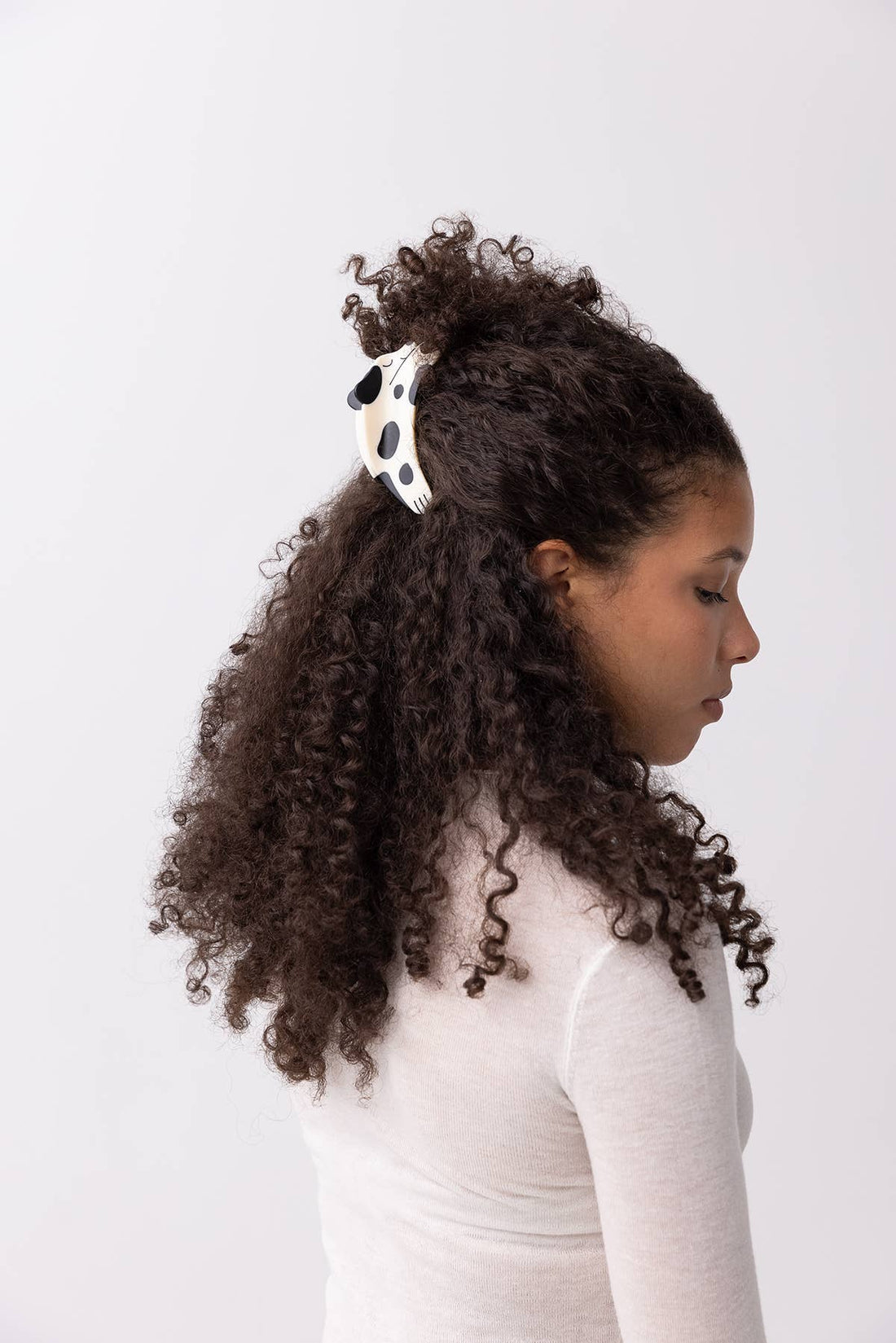 Puppy Claw hair clip, white and black spotted matte acetate, worn on dark curly hair in a half-up style, side view