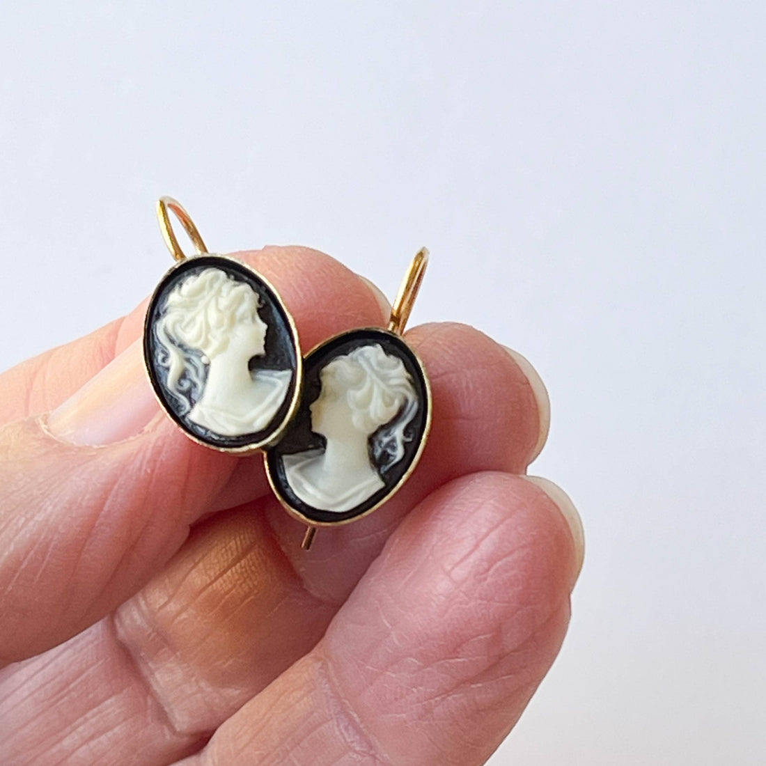 Small Black Cameo earrings, white resin cameo on black, 24K antiqued gold-plated setting, held in hand for scale.