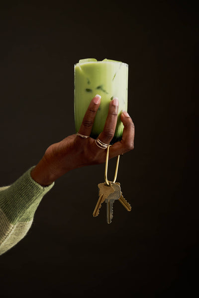 
                    
                      Ceremonial Matcha iced drink, vibrant green with ice, held in hand with a brass key loop
                    
                  