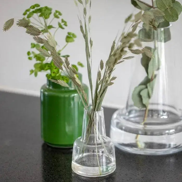 Flora mouth-blown glass vase, clear, small size, with dried grasses, styled in foreground among other vases.