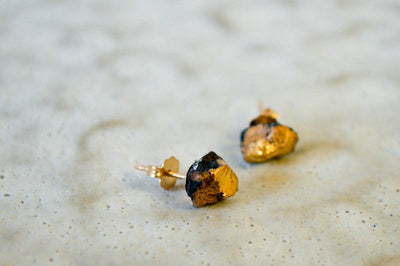 
                    
                      Gold Ore Studs stud earrings, black porcelain with 22k gold luster, close-up on textured surface showing gold posts.
                    
                  