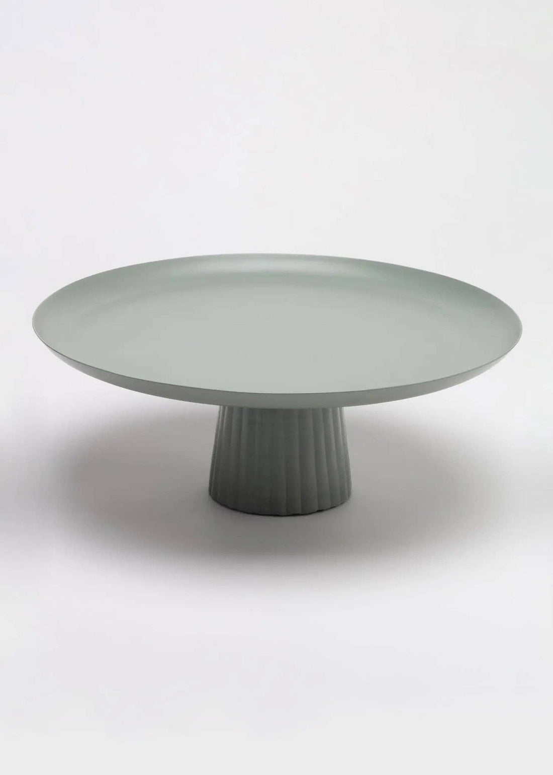 Avisa cake stand, sage green powder-coated metal with ribbed base, angled view on white.