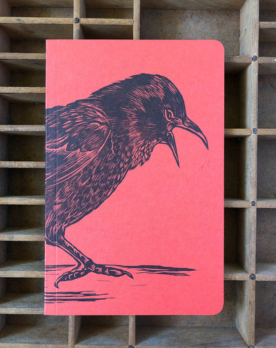 
                    
                      Crow Large Letterpress notebook, coral red paper cover with striking black crow illustration and open beak, front view.
                    
                  