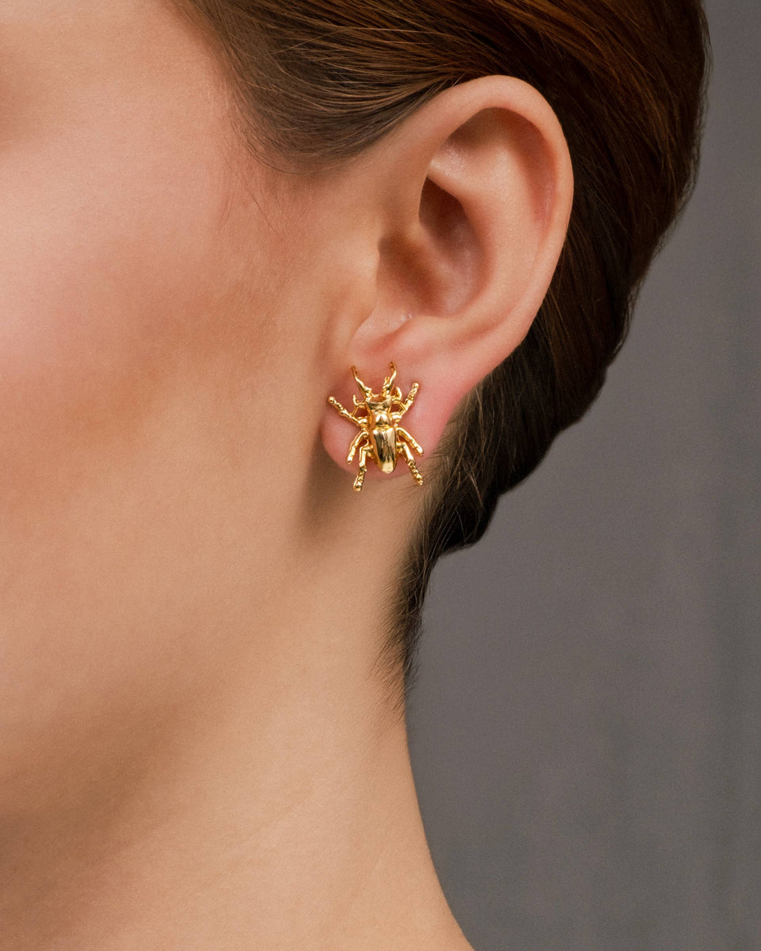 Gold Beetle stud earrings, shiny gold, on ear close-up.