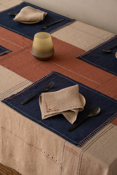 
                    
                      Linen Fern Napkin Set, Sandy Beige European linen, folded on dark placemat showing decorative stitching detail.
                    
                  