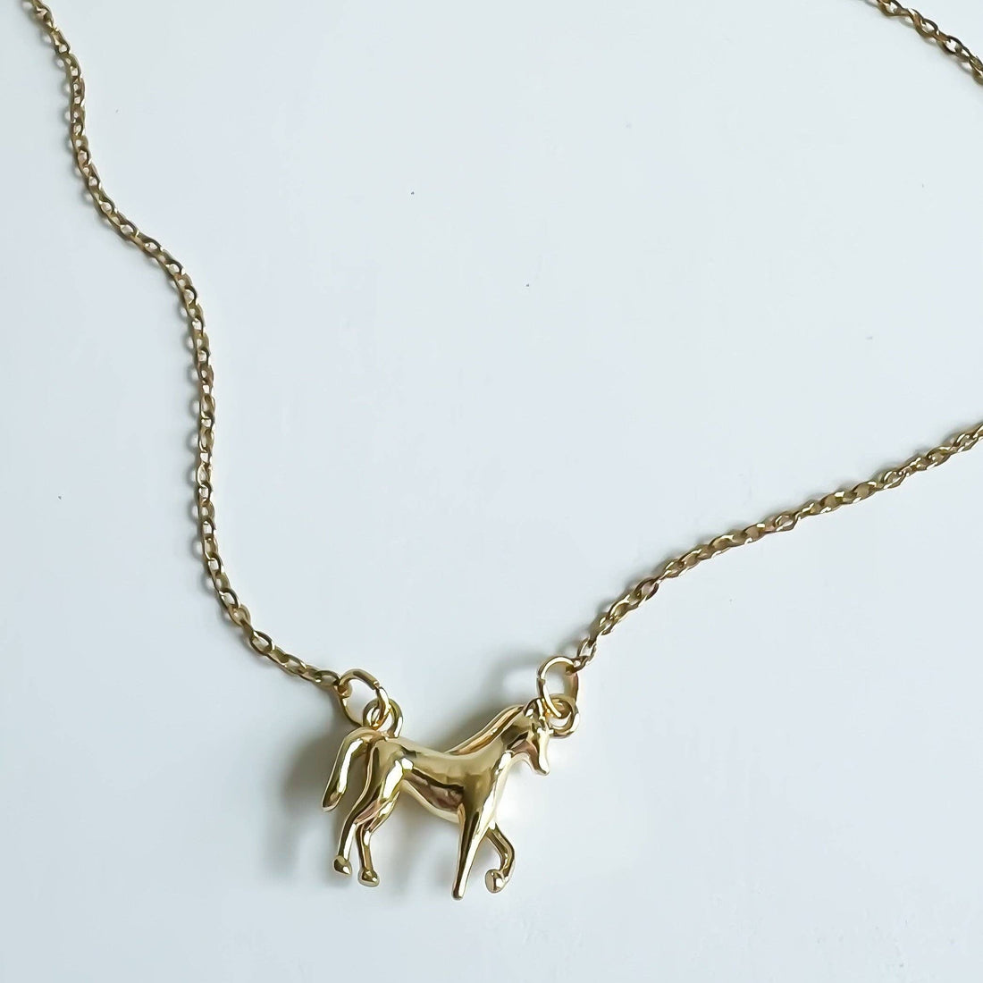 Gold Horse Girl necklace, close-up of the sculptural horse pendant and fine link chain, flat lay on white.