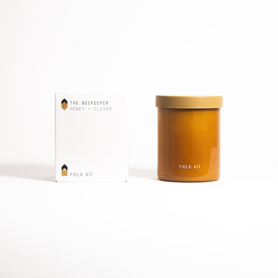The Beekeeper Honey + Clover glass candle, warm honey-colored jar with lid, displayed next to its white product box.
