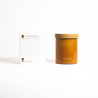 
                    
                      The Beekeeper Honey + Clover glass candle, warm honey-colored jar with lid, displayed next to its white product box.
                    
                  