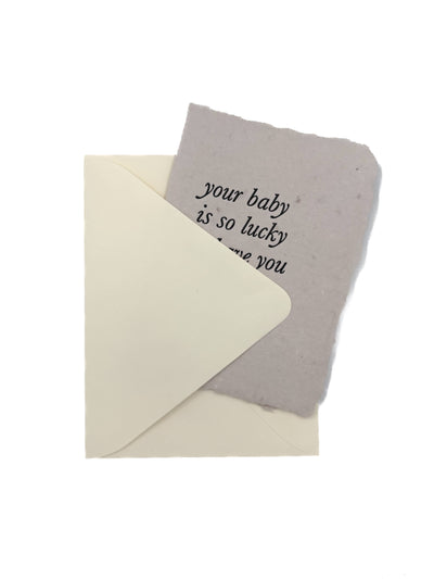 
                    
                      "Your Baby Is So Lucky" greeting card, grey handmade paper with ragged edge, partially tucked into a cream envelope.
                    
                  