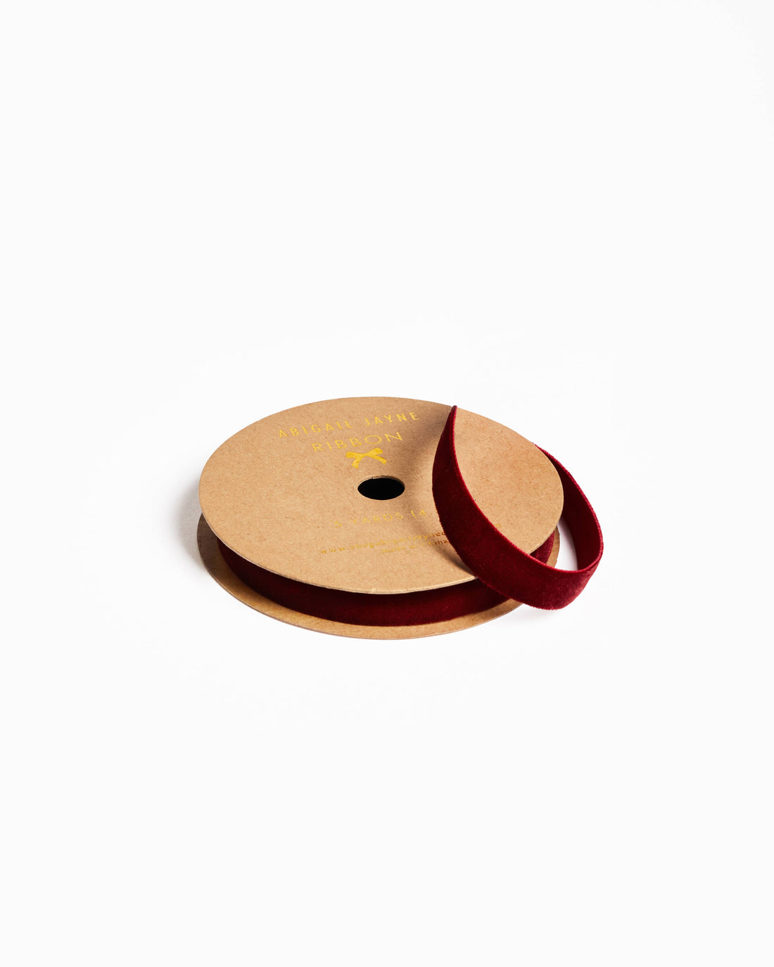 Garnet velvet ribbon on kraft paper spool, partially unwound with ribbon loop, angled view.