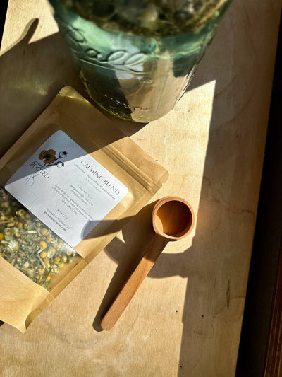 
                    
                      Wooden Tea Scoop, unfinished beechwood, angled view showing the scoop bowl next to a tea pouch on a light wood surface.
                    
                  