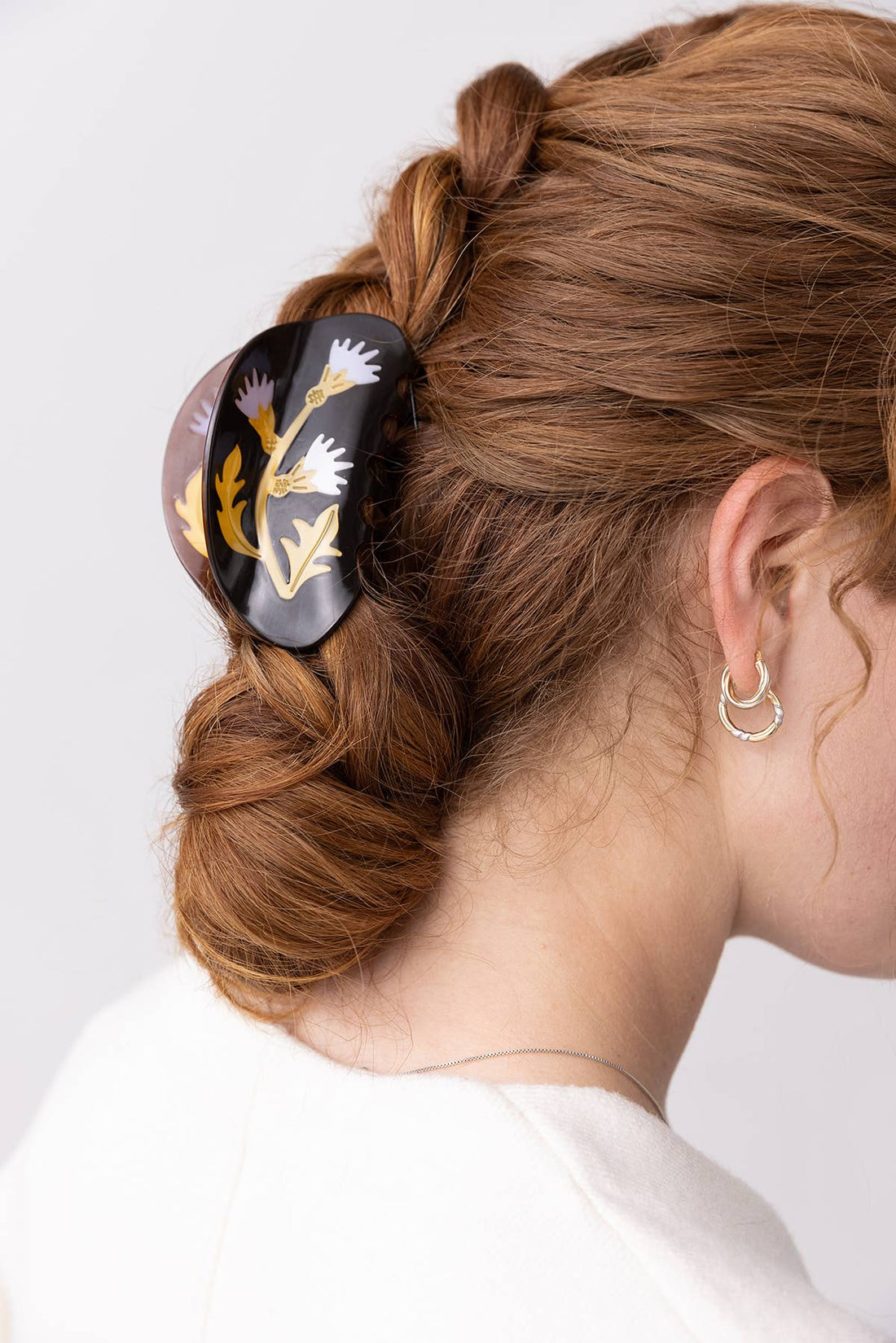 Milk Thistle Hair Claw, dark acetate with purple, white, gold thistle pattern, worn holding braided bun, side view.