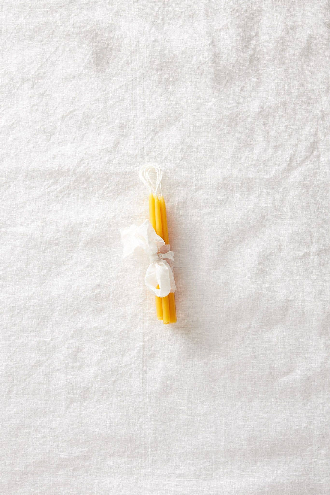 Traditional Beeswax Birthday Candles, yellow pure beeswax, tied with white tissue, flat lay on white linen.