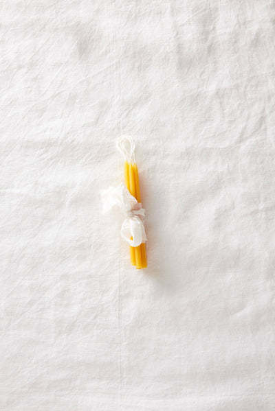 
                    
                      Traditional Beeswax Birthday Candles, yellow pure beeswax, tied with white tissue, flat lay on white linen.
                    
                  