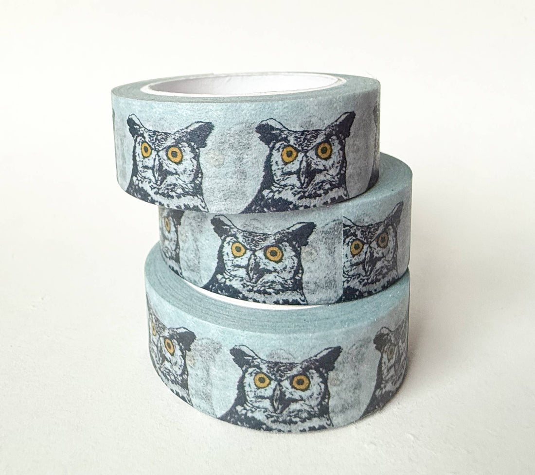 Great Horned Owl washi tape, three stacked rolls, grey-blue with repeating black, white, and yellow owl faces, angled view.