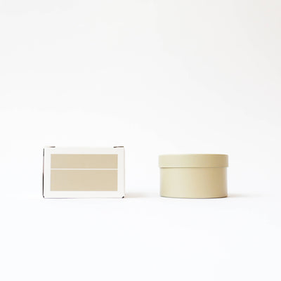 
                    
                      The Librarian tin candle, light beige, next to its white packaging box with a beige label, front view.
                    
                  