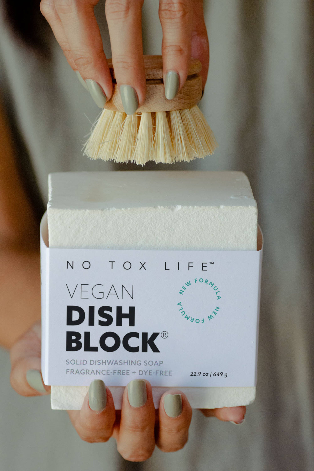 Dish Block Solid Dish Soap, white bar with label, held by hands with a wooden scrub brush poised above.
