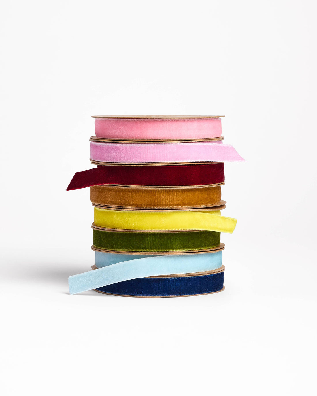 Rose pink velvet ribbon spool within a stack of diverse colorful velvet ribbons, front view.