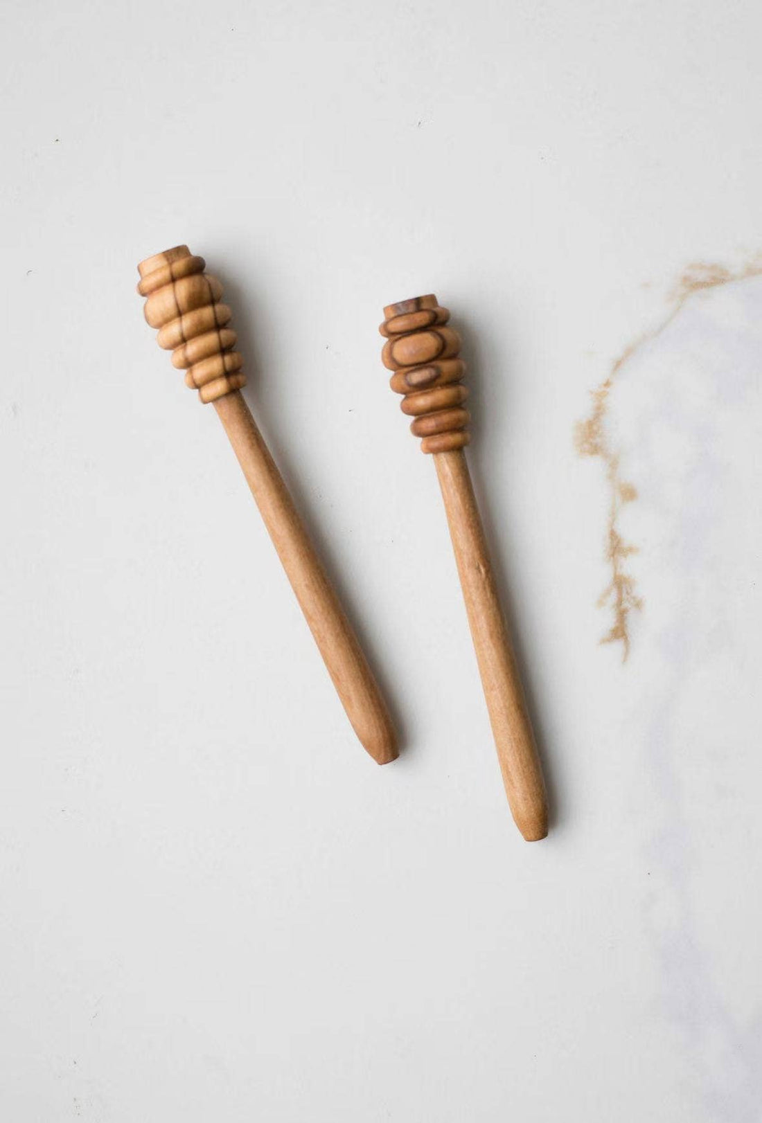 Fodory Olive Wood Honey Dipper, natural light brown olive wood, pair angled flat lay on a subtle marble surface.
