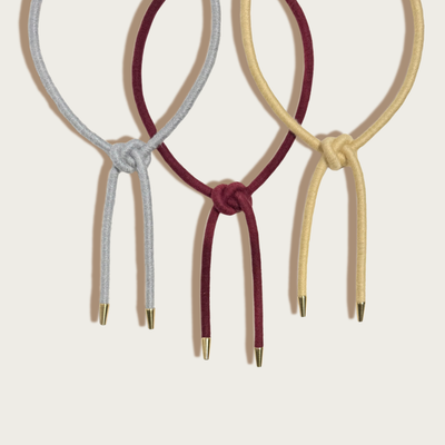 
                    
                      Three Shoelace Square Knot Bolo ties: grey, burgundy, and buttercream wool-wrapped nylon with raw brass tips, close-up group…
                    
                  