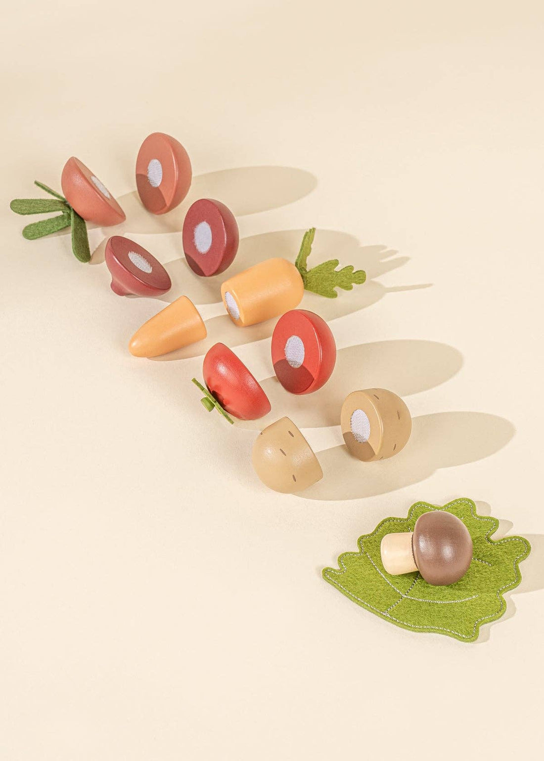 Wooden Vegetables Playset showing brown, orange, red wooden pieces, cut in half and scattered with green felt leaves.
