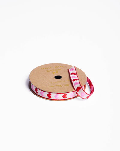 
                    
                      Hearts woven ribbon, white fabric with alternating pink and red embroidered hearts and red trim, close-up on spool.
                    
                  