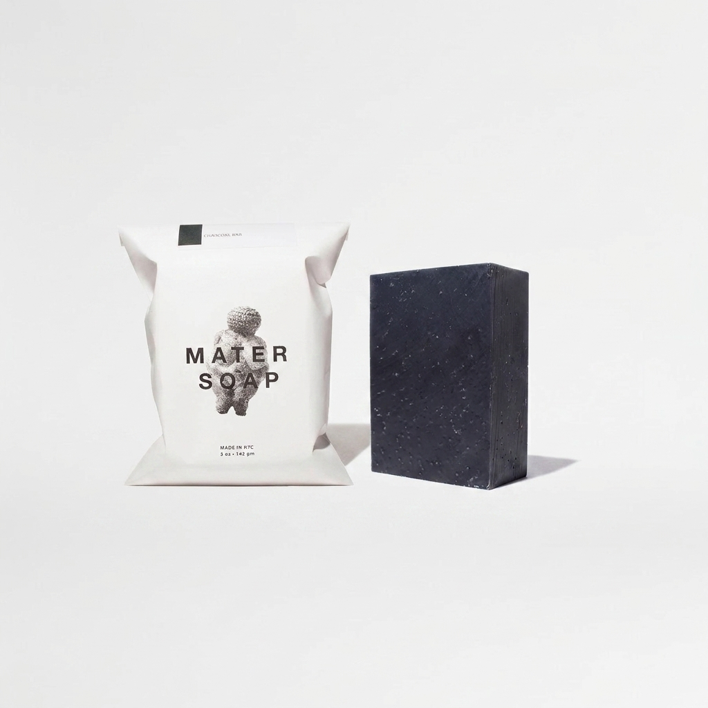 Mater Soap Charcoal Soap Bar, dark grey speckled bar and white paper packaging, front view on white.