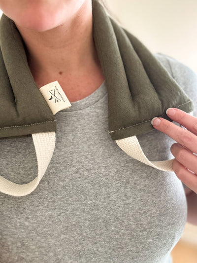 
                    
                      Olive Microwaveable Neck Wrap on neck, close-up showing cotton-linen fabric texture, natural strap, and small brand tag.
                    
                  