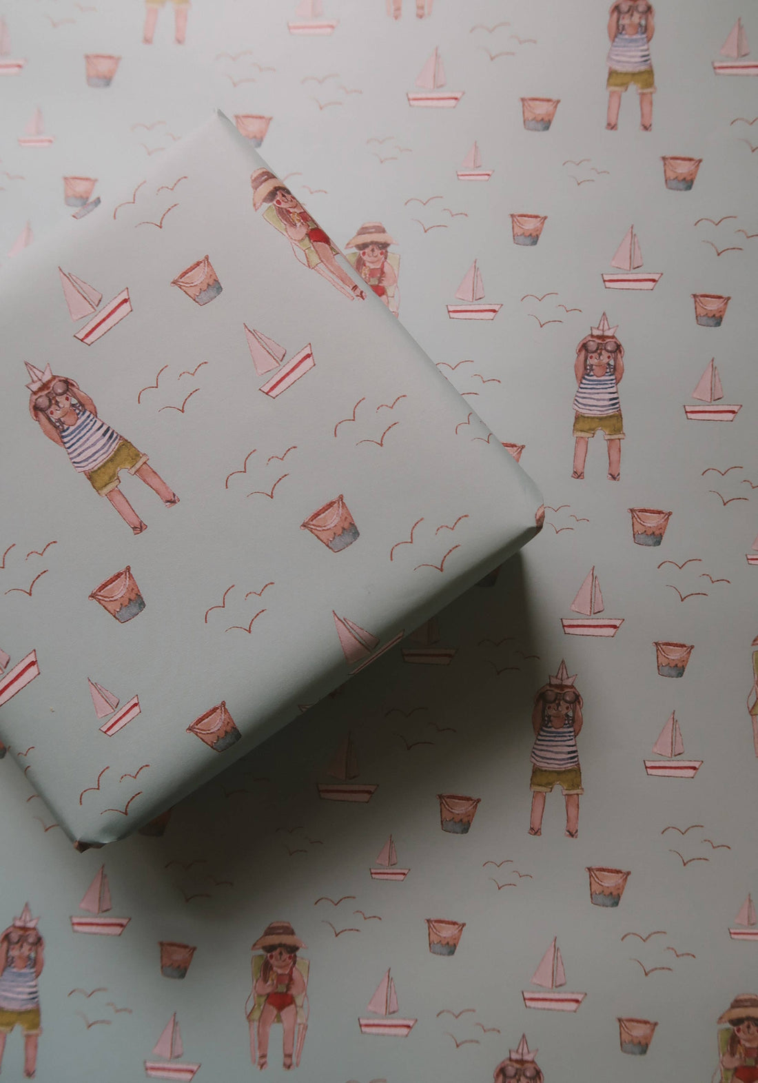 Agnese Grīnberga's Summer Wrapping Paper, light blue pattern with boats, buckets, and cartoon animals, layered diagonal view.