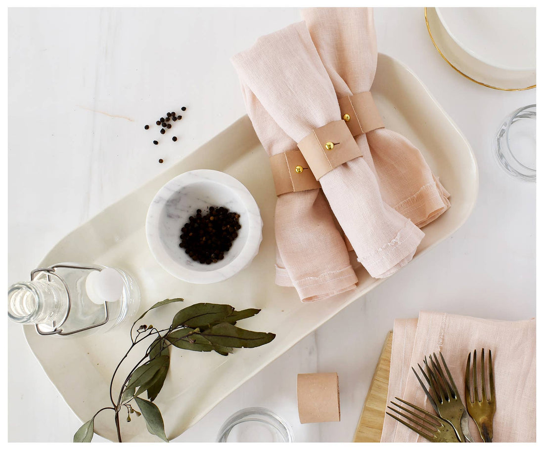 Tan Leather Napkin Rings, set of 4, close-up of tan leather with brass clips, styled on pink linen napkins, flat lay.