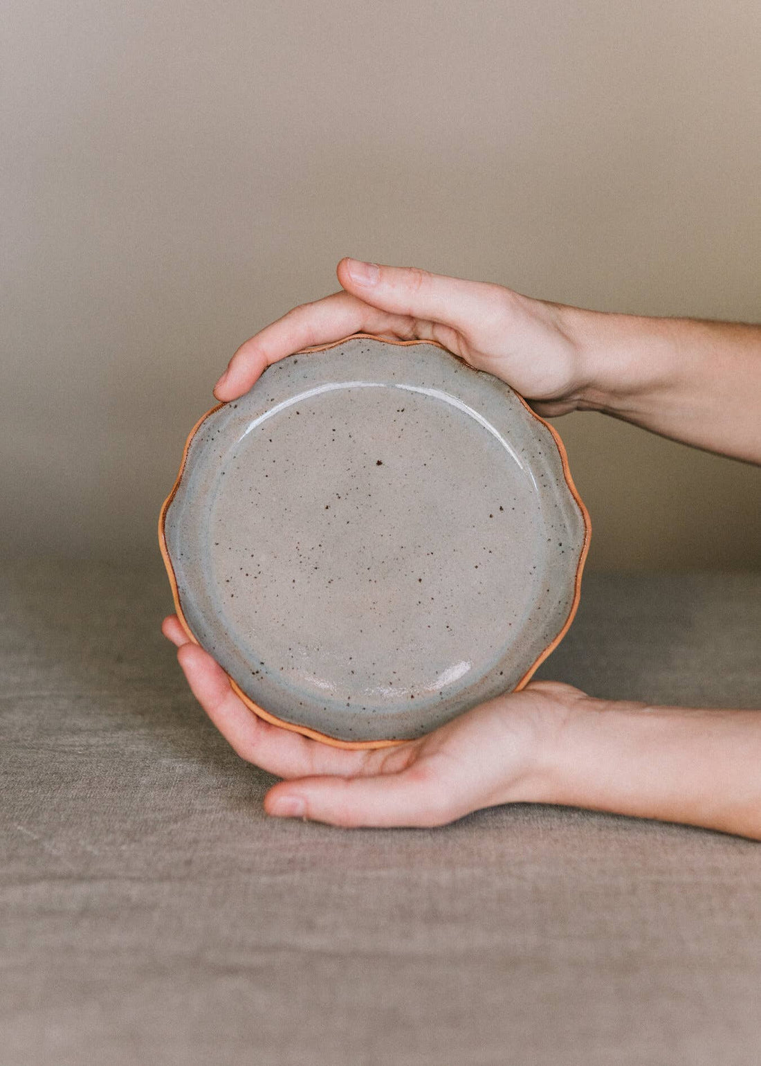Handcrafted Stoneware Plate, speckled gray, with wavy raw brown rim, held in hands for scale and detail.