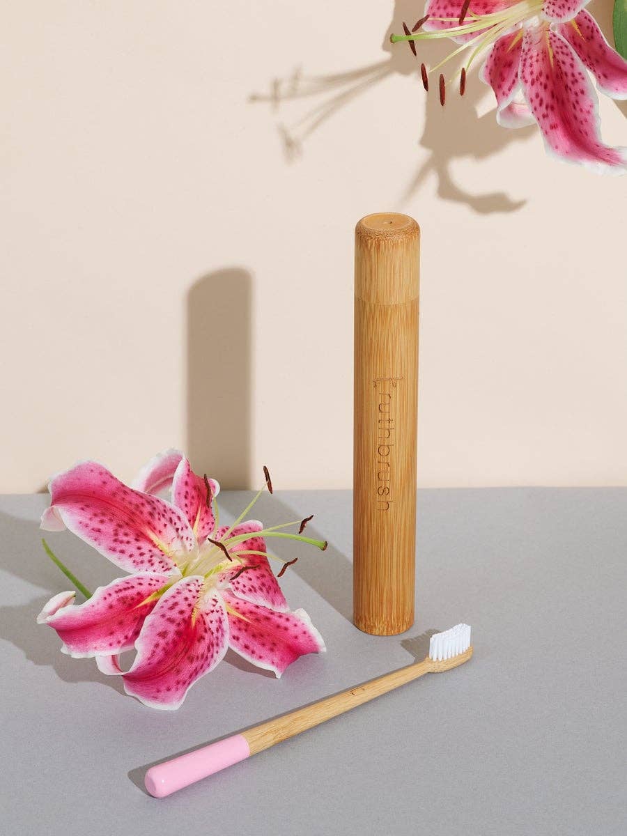 Petal Pink Bamboo Toothbrush with pink tip, white bristles, natural bamboo handle, beside a bamboo travel case, flat lay.