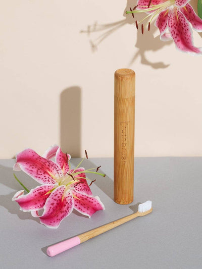
                    
                      Petal Pink Bamboo Toothbrush with pink tip, white bristles, natural bamboo handle, beside a bamboo travel case, flat lay.
                    
                  
