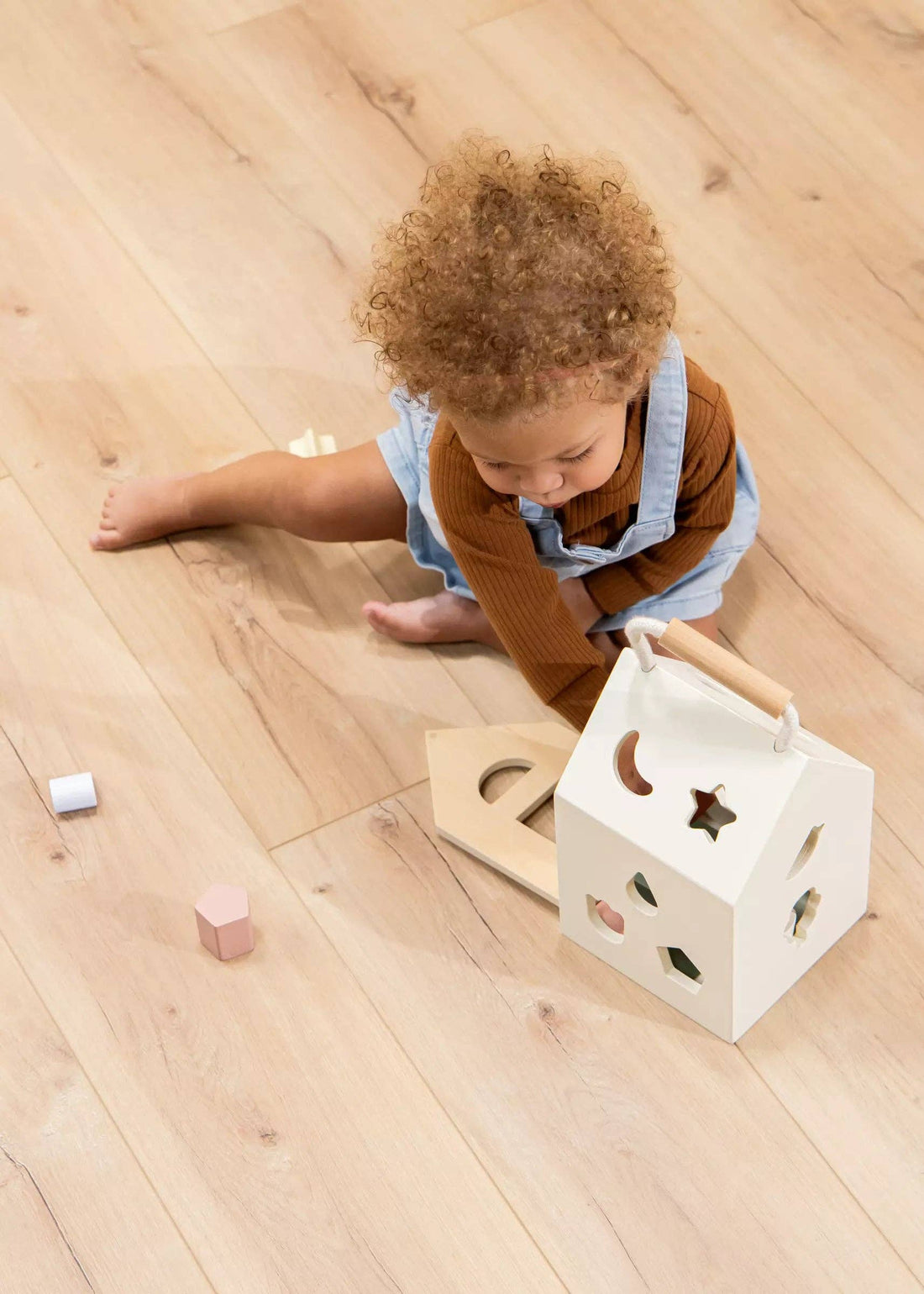 Sorting House wooden shape sorter, white wood house, natural wood handle, baby playing with pink and white shapes.