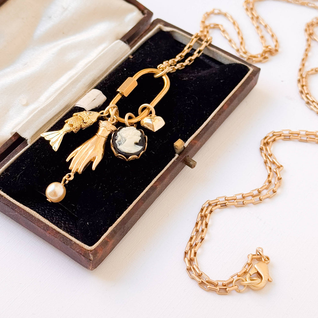 Gold Carabiner Charm Necklace with fish, hand, cameo, pearl, and heart charms, in velvet box, gold chain detail.