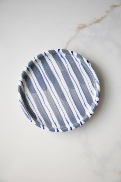 
                    
                      Striped ceramic plate, white with hand-painted irregular diagonal grey-blue stripes, angled top view on marble surface.
                    
                  