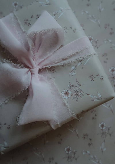 
                    
                      Vintage Blooms illustrated wrapping paper, beige floral pattern, close-up of a gift wrapped with a soft pink frayed ribbon.
                    
                  