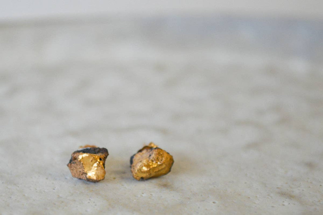 Gold Ore stud earrings, hand-formed dark porcelain with 22k gold luster, flat lay pair showing organic texture.