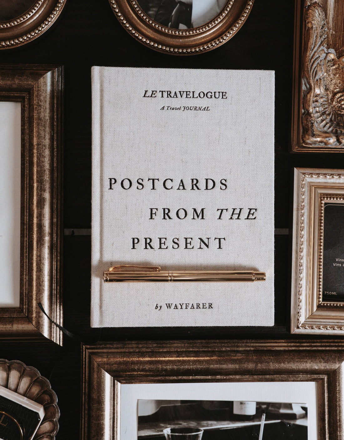 Wayfarer Postcards from the Present Travel Journal, light linen cover, with a gold pen resting on it, flat lay among ornate…