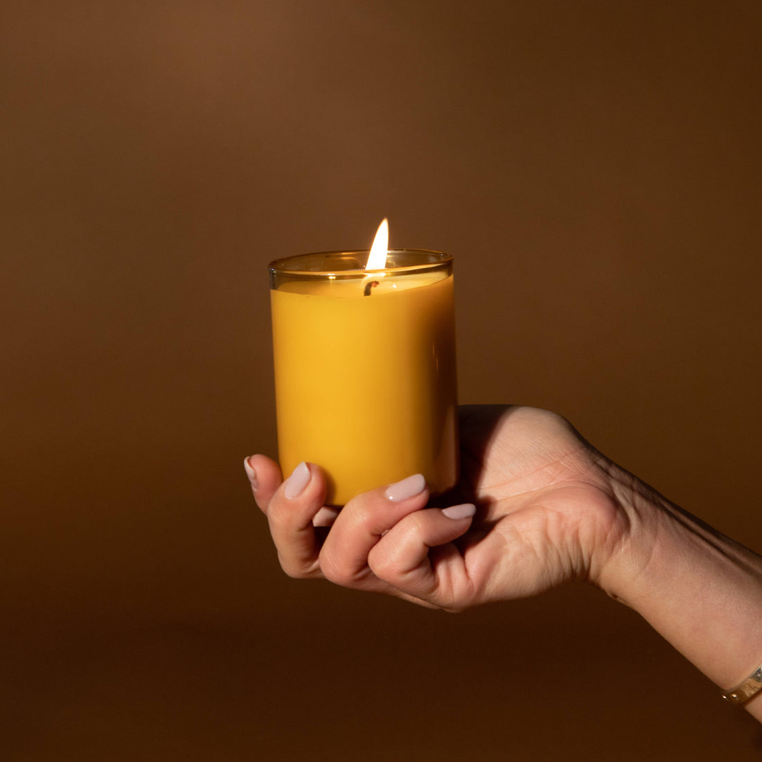 The Beekeeper Glass Candle, honey-colored soy wax, held in hand with flame lit for scale.