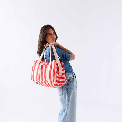 
                    
                      Raphael cotton Weekend Bag, vertical tomato & candy pink stripes, carried on shoulder by person, playful wink.
                    
                  