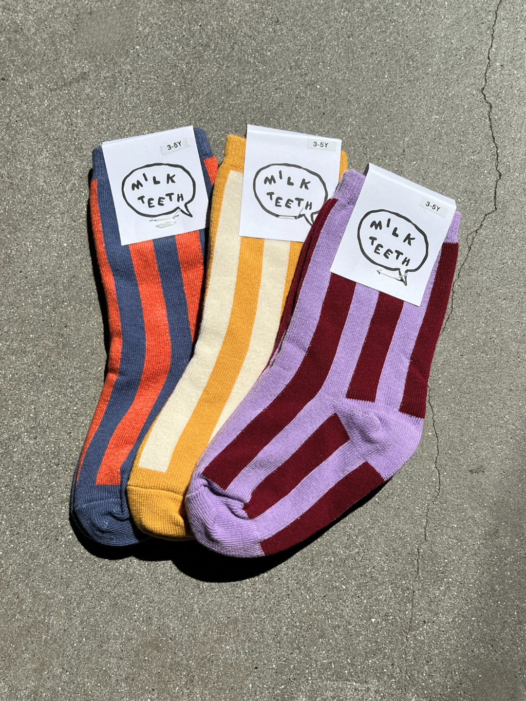 Kids Stripe Sock cotton socks, three folded pairs in blue/orange, yellow/cream, purple/burgundy stripes, 3-5Y tags, flat lay.