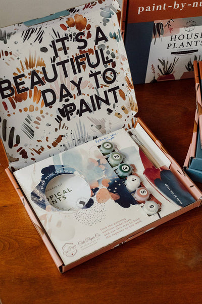 
                    
                      Peony Blossoms Paint-by-Numbers Kit, open Cate Paper Co. box, 'IT'S A BEAUTIFUL DAY TO PAINT' lid, showing acrylic paint…
                    
                  