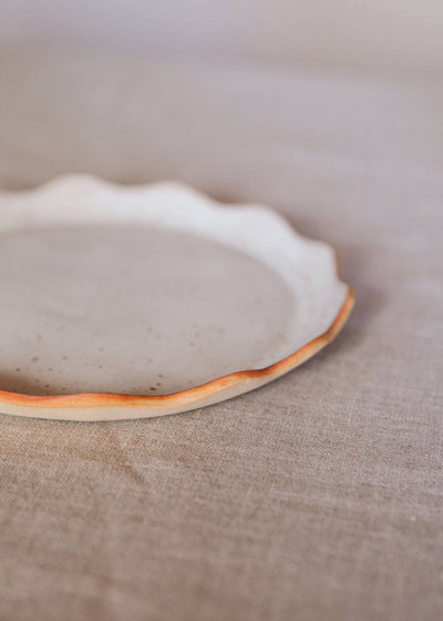 
                    
                      Handcrafted Stoneware Plates, close-up showing wavy edge, speckled stoneware surface, and orange-brown rim.
                    
                  