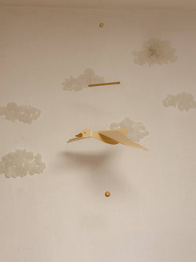 
                    
                      Wooden Flying Goose Mobile, natural wood with white collar, side view hanging from its bar, against a subtle cloud-painted…
                    
                  