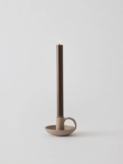 
                    
                      Nimo candle holder, matte speckled stoneware with side handle, holding a lit brown taper candle, front view.
                    
                  